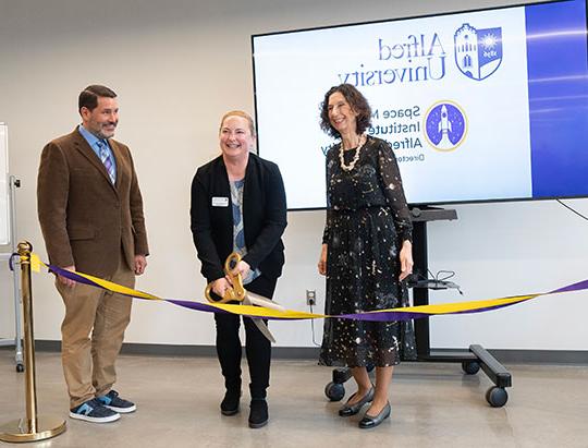 three people, two women and a man, one woman using giant scissors to cut a ribbon